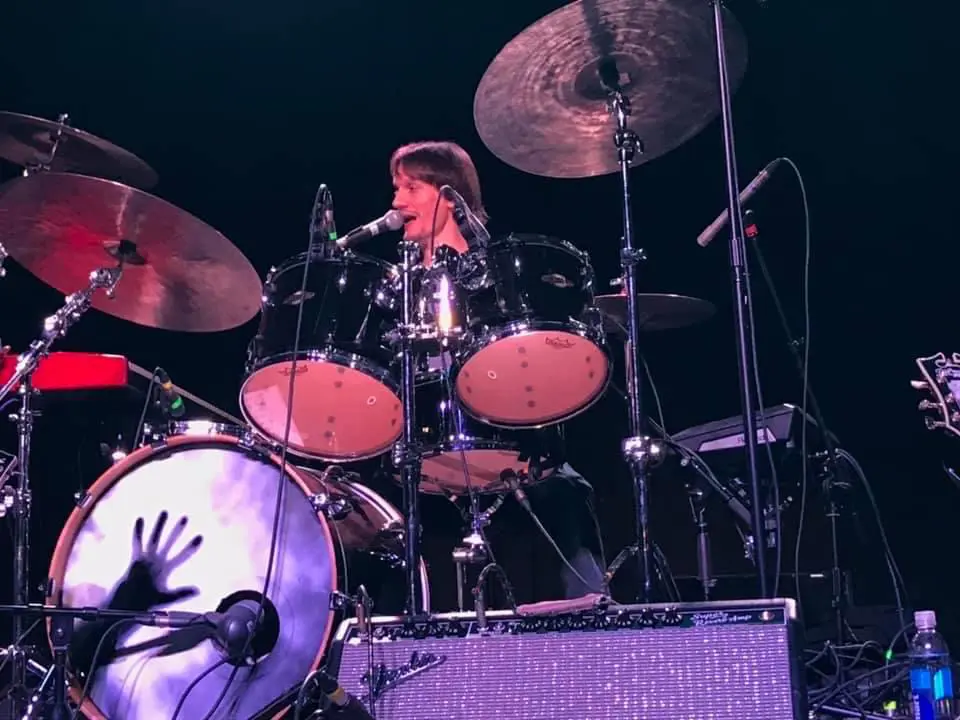 A man playing drums on stage with other people.